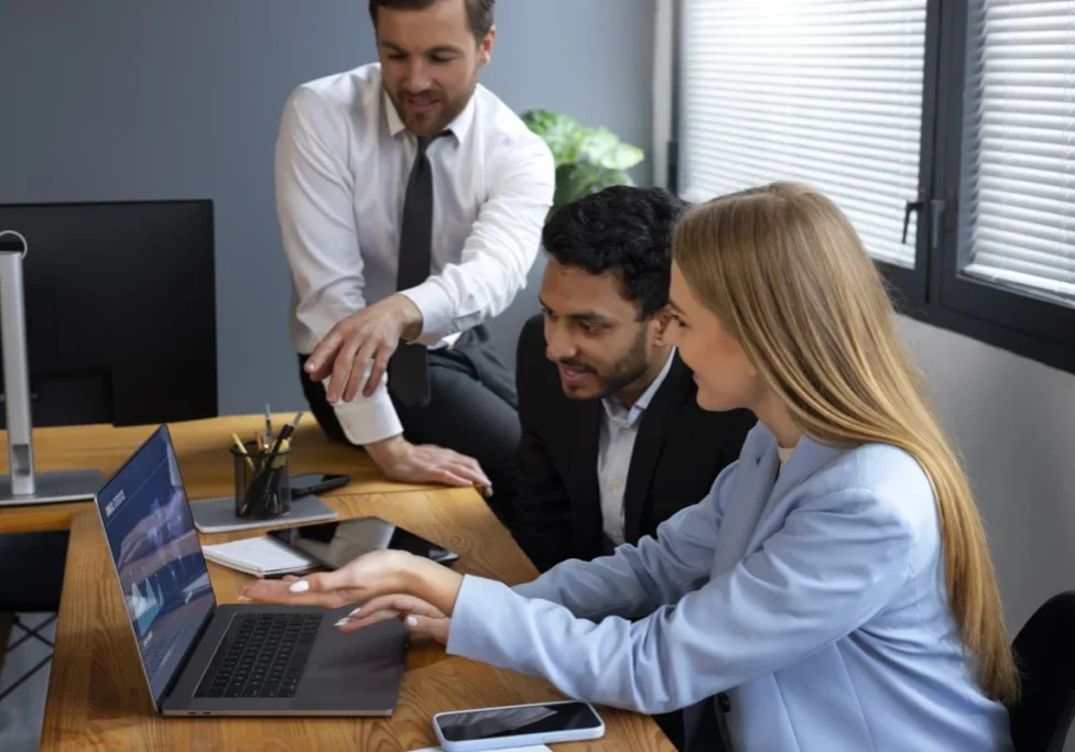 A group of people sitting around a table with laptops.